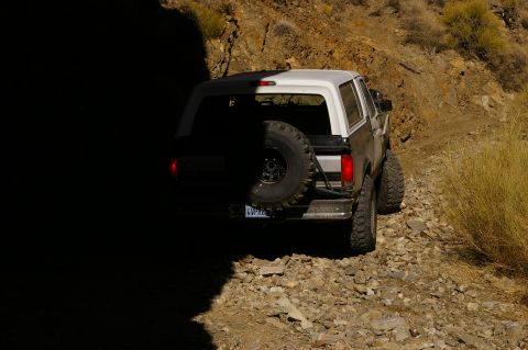 1986 Ford Bronco - This Ford Bronco is navigating a rough, unpaved path with dry brush and rocky terrain.