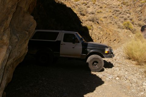 1986 Ford Bronco - Ford Bronco navigates a tight, rocky path in a desert canyon.