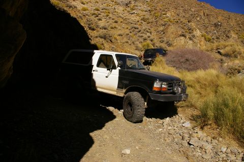 1986 Ford Bronco - A two-tone Ford Bronco navigates a rough, mountainous terrain with another vehicle visible in the background.
