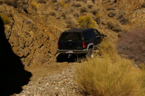1986 Ford Bronco - A black Chevrolet Tahoe navigates a , off-road path with dry brush and rocky terrain.