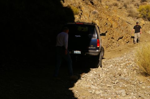 1986 Ford Bronco - A blue Chevrolet SUV navigates a rocky, off-road path with two people nearby.