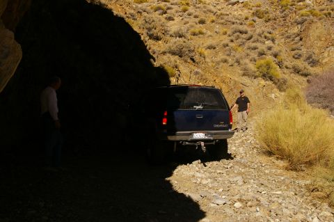 1986 Ford Bronco - Chevrolet SUV on a rough road, partially in shadow near a cave opening.