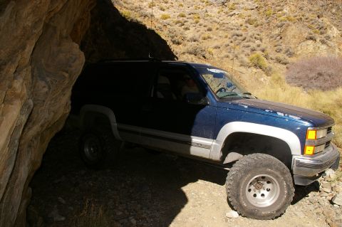 1986 Ford Bronco - A blue SUV navigates a narrow, rocky passage, its tires kicking up dust.