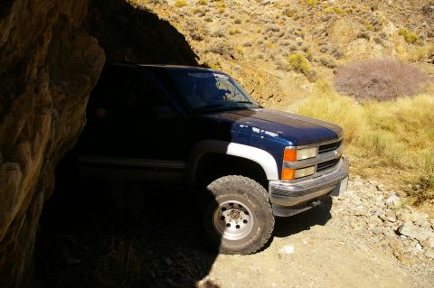 1986 Ford Bronco - A pickup truck is parked on a dirt road, partially obscured by a rock formation, with dry brush in the background.