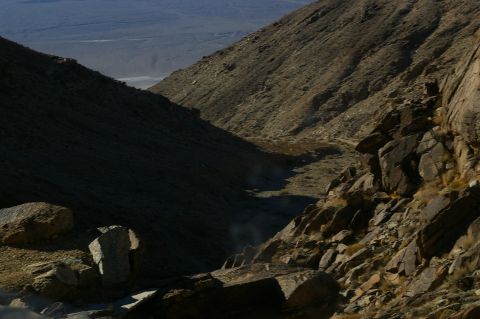 1986 Ford Bronco - A vast desert canyon landscape under a clear sky, with , rocky slopes and a dry riverbed winding through the terrain.
