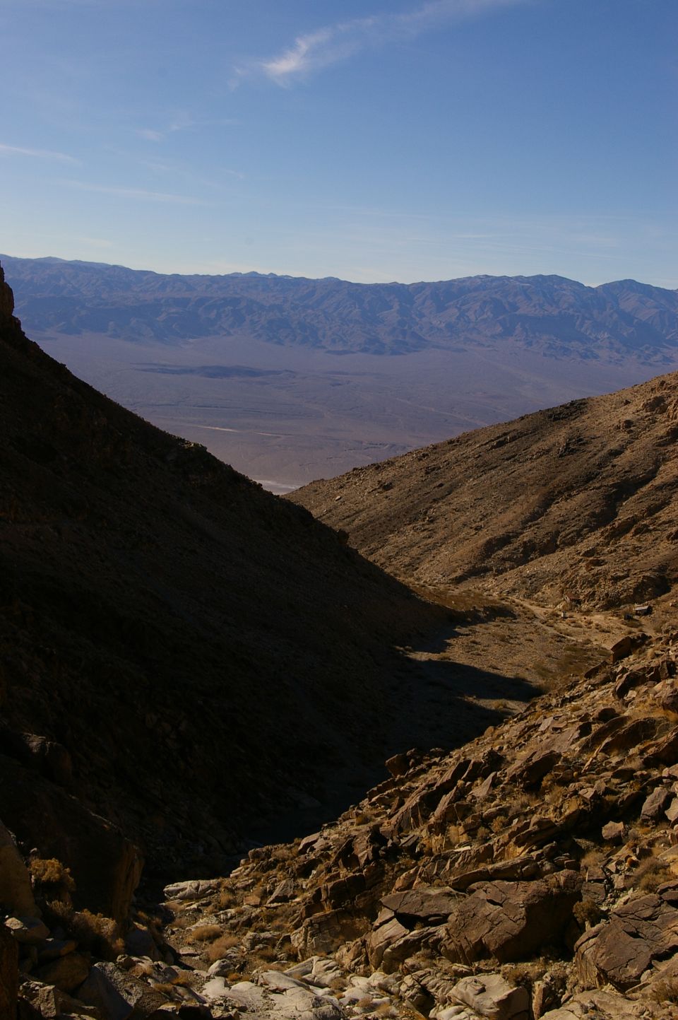 Desert canyon with rocky slopes and distant mountains under a clear blue sky