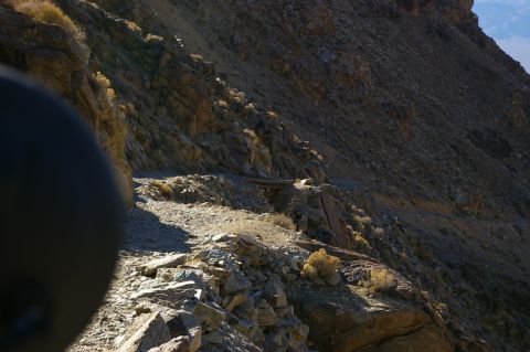 1986 Ford Bronco - A rocky mountain road winds through a desolate landscape, with a dark object partially obscuring the view in the foreground.