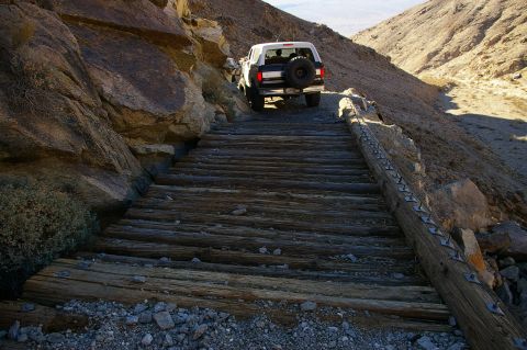 1986 Ford Bronco - A Ford Bronco navigates a precarious wooden bridge on a steep, rocky incline.