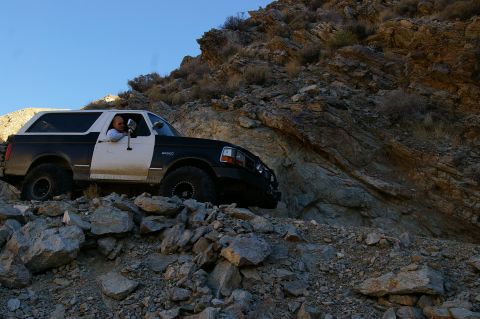 1986 Ford Bronco - A Ford Bronco navigates a steep, rocky incline under a clear blue sky.