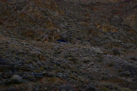 1986 Ford Bronco - A dark blue 1986 Ford Bronco navigates a , rocky terrain under a dim sky.