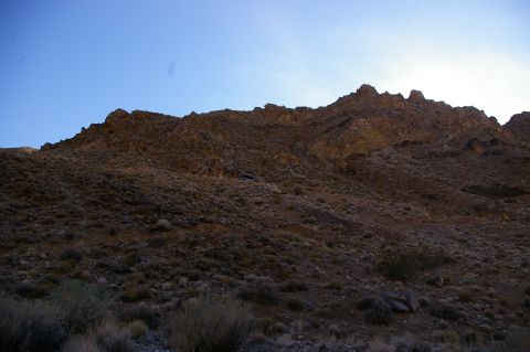 1986 Ford Bronco - Dry brush and rocks cover a steep, rocky hillside under a bright blue sky.