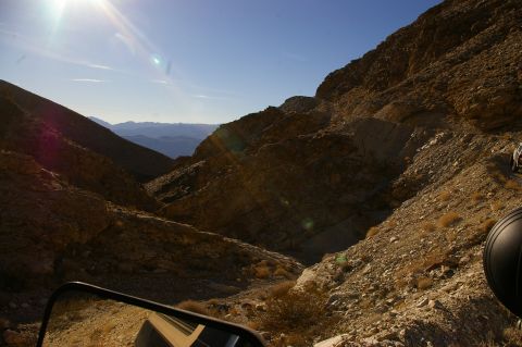 1986 Ford Bronco - Driving through a mountain pass with a clear blue sky and sun glare.
