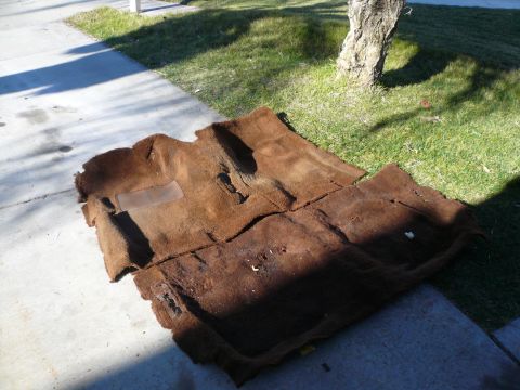 1975 Ford Ranchero - Car carpet removed from a vehicle lies on the ground outside.