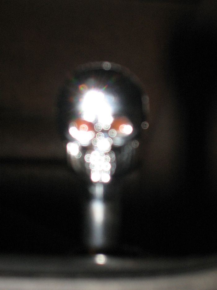 Blurry close-up of a chrome skull ornament with bright light reflections in a dark setting