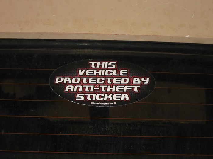 Oval anti-theft sticker on a dark vehicle window with horizontal defroster lines