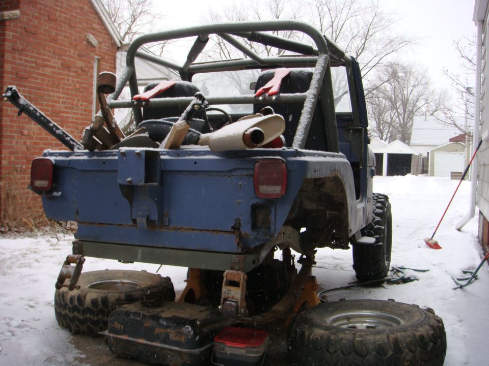 Blue Jeep CJ5 rear view, on jack stands with spare tires. Roll cage visible