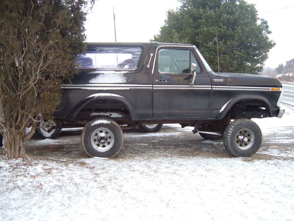 1979 Ford Bronco parked in snow, side view. Black paint with chrome trim
