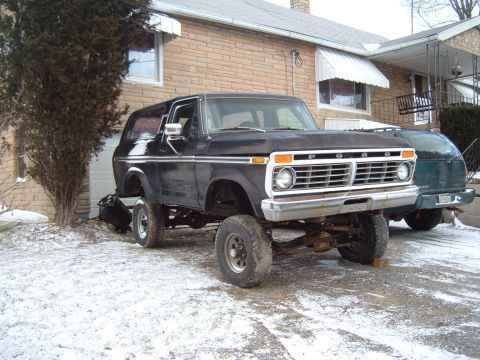 1979 Ford Bronco - This lifted black Ford Bronco is parked in a snowy driveway next to another vehicle.