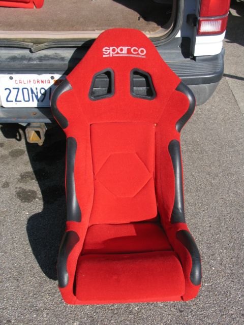 1984 Ford Bronco - Sparco racing seat is shown in front of a vehicle's rear. California license plate is visible.