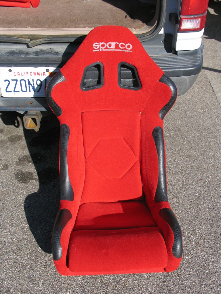 Sparco racing seat, red with black trim, in front of a vehicle tailgate and California license plate