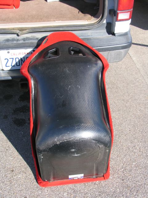 1984 Ford Bronco - A racing seat is placed on the ground next to the rear of a vehicle, with its tailgate open.