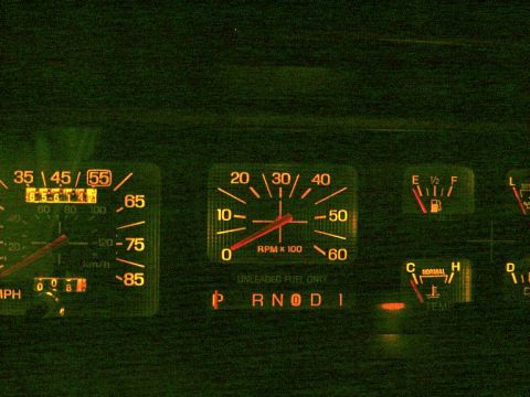 1986 Ford Bronco - Nighttime close-up of an illuminated instrument cluster glowing green and orange, showing a speedometer (with 55 mph highlighted), a tachom…