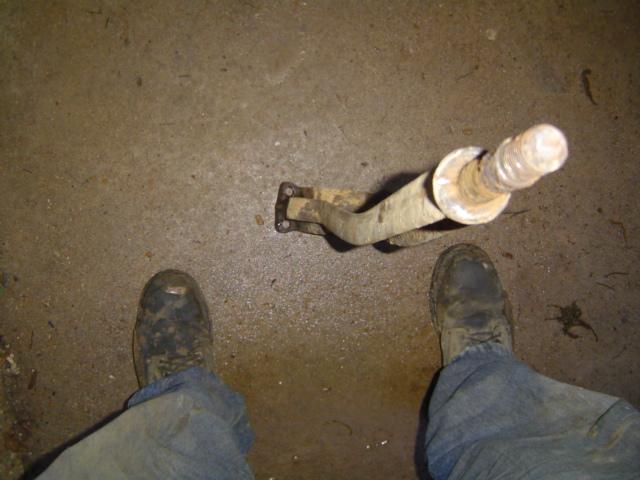 Rusty metal part with a threaded bolt and two feet in work boots on concrete