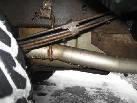 1996 Ford Bronco - Close-up of brake lines and exhaust pipe under a vehicle, with snow visible.