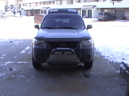 2006 Ford Escape - A silver 2006 Ford Escape is parked in front of buildings with snow on the ground. Another vehicle is visible in the background.