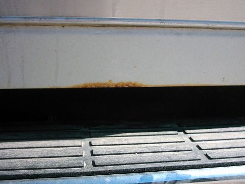 1987 Ford Bronco - Close-up view of rust forming on the lower body panel and step of a white vehicle.