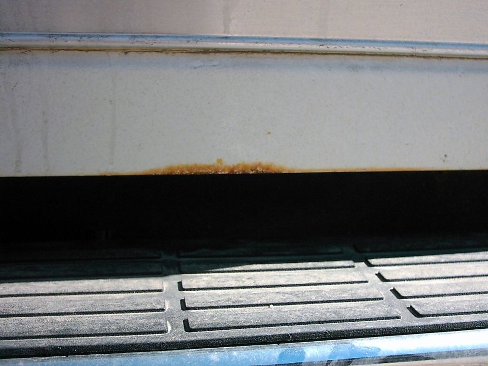Rust on lower body panel and step of a white vehicle