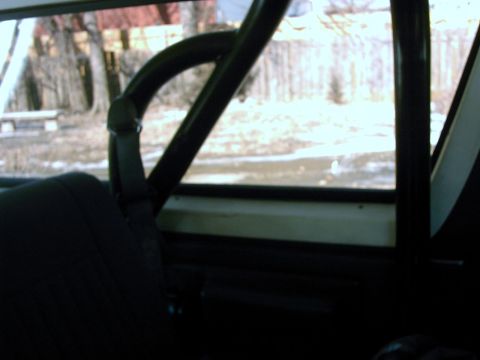 1987 Ford Bronco - Interior view shows a roll cage and seat, with a blurry outdoor scene visible through the window.