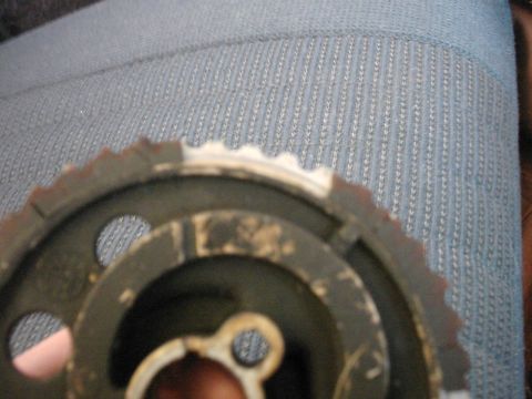 1987 Ford Bronco - A close-up view of a worn metal timing gear, with a blue fabric surface in the background.