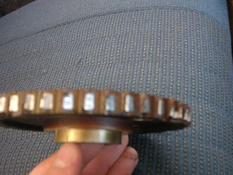 1987 Ford Bronco - A close-up view of a metal gear, likely a timing gear, held by a hand against a blue, textured background.