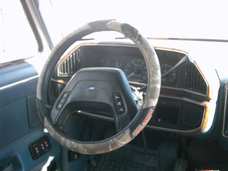 1987 Ford Bronco interior showing steering wheel with camo cover, dashboard, and door panel