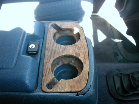 1987 Ford Bronco - The interior of the vehicle shows a worn wooden trim around the center console cupholders.