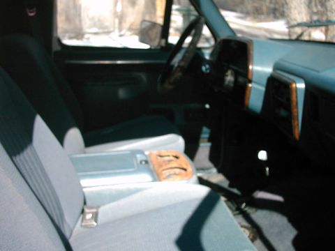 1987 Ford Bronco - The interior of this truck shows a dashboard with wood trim and light blue upholstery on the seats.