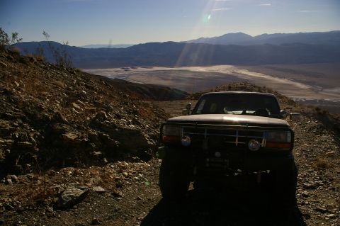 1986 Ford Bronco - A 1987 Ford Bronco is parked on a rocky desert trail overlooking a dry lake bed.