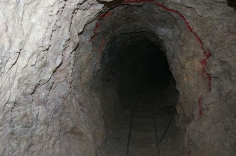 1986 Ford Bronco - A dark mine tunnel with tracks running along the floor and red markings on the rough rock walls.