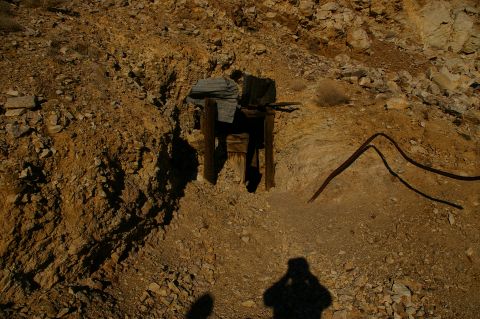1986 Ford Bronco - A view of an old mine entrance in a desolate, rocky terrain, with a photographer's shadow cast on the ground.