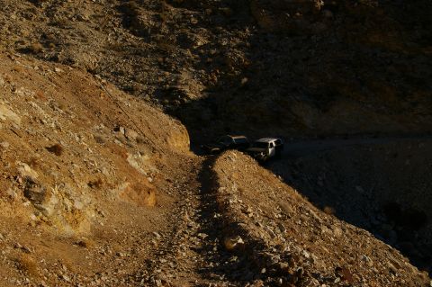 1986 Ford Bronco - Two vehicles navigate a steep, rocky trail under harsh sunlight, highlighting the terrain.