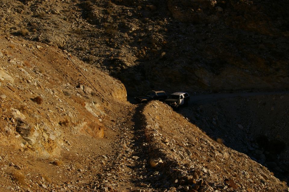 Two SUVs parked on a narrow dirt road in a rocky, mountainous desert landscape