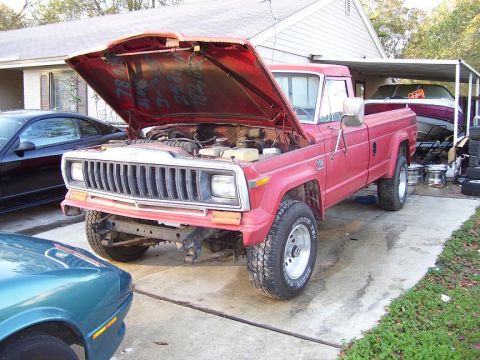 2004 Jeep TJ - Red Jeep J-10 pickup truck with its hood open, parked in a driveway next to another car and a boat.