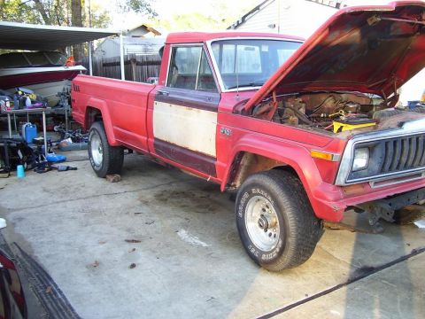2004 Jeep TJ - A red pickup truck with its hood open sits in a driveway, revealing its engine and a yellow battery box.