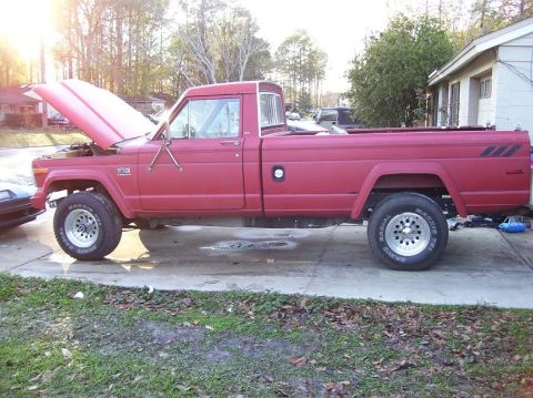 2004 Jeep TJ - This red Jeep pickup truck, seen from the side with its hood open, has styling cues that suggest it is from the 1980s, not 2004.