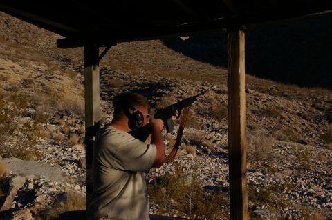 1986 Ford Bronco - Man at outdoor shooting range aims rifle. Desert terrain visible behind him.
