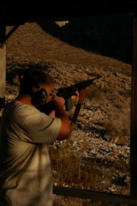 1986 Ford Bronco - A man takes aim with a rifle from a covered shooting position overlooking a rocky hillside.