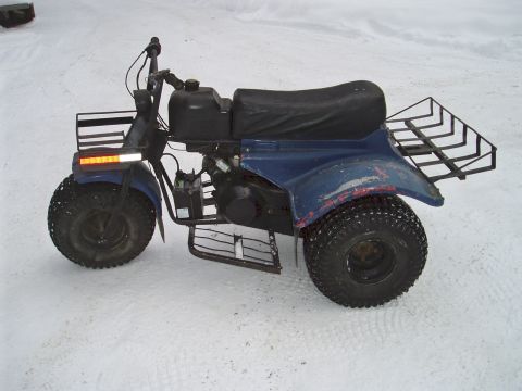 2000 Ford E350 - Side view of a weathered blue three-wheeler ATC parked on packed snow, with faded and scratched bodywork, a long black bench seat and a bla…