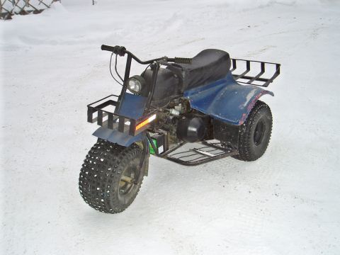 2000 Ford E350 - A blue three-wheeled ATV sits in a snowy landscape, equipped with front and rear cargo racks.