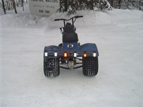 2000 Ford E350 - Straight-on rear view of a weathered blue three-wheeled ATC parked on packed snow, showing the wide rear fender with a row of white and red…